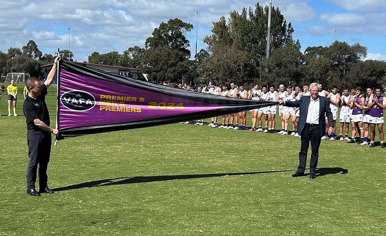 Life members David Southgate and Peter Bowring unfurl the 2024 premiership flag before the Bloods' season opener against Collegians