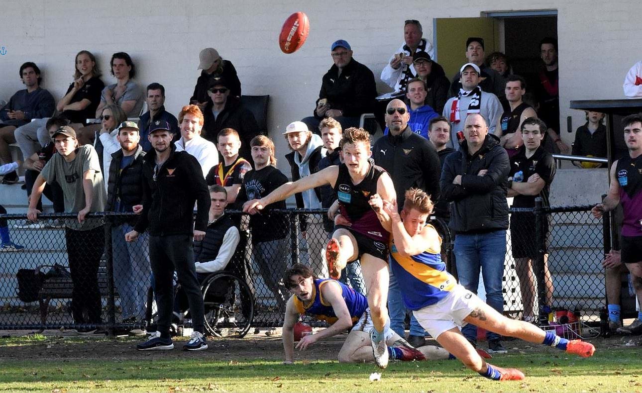 Rayner Seccull clears from defence watched by the Throng, including the coaches bench and club legend Hyxy in the background with a sly pie