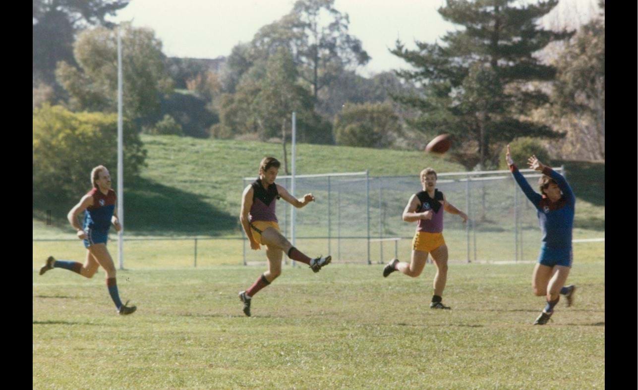 Mark Newton, neat as ever, streams out of the backline in his hundredth game watched by Tony “Perce” Mitchem at Banyule, 1986