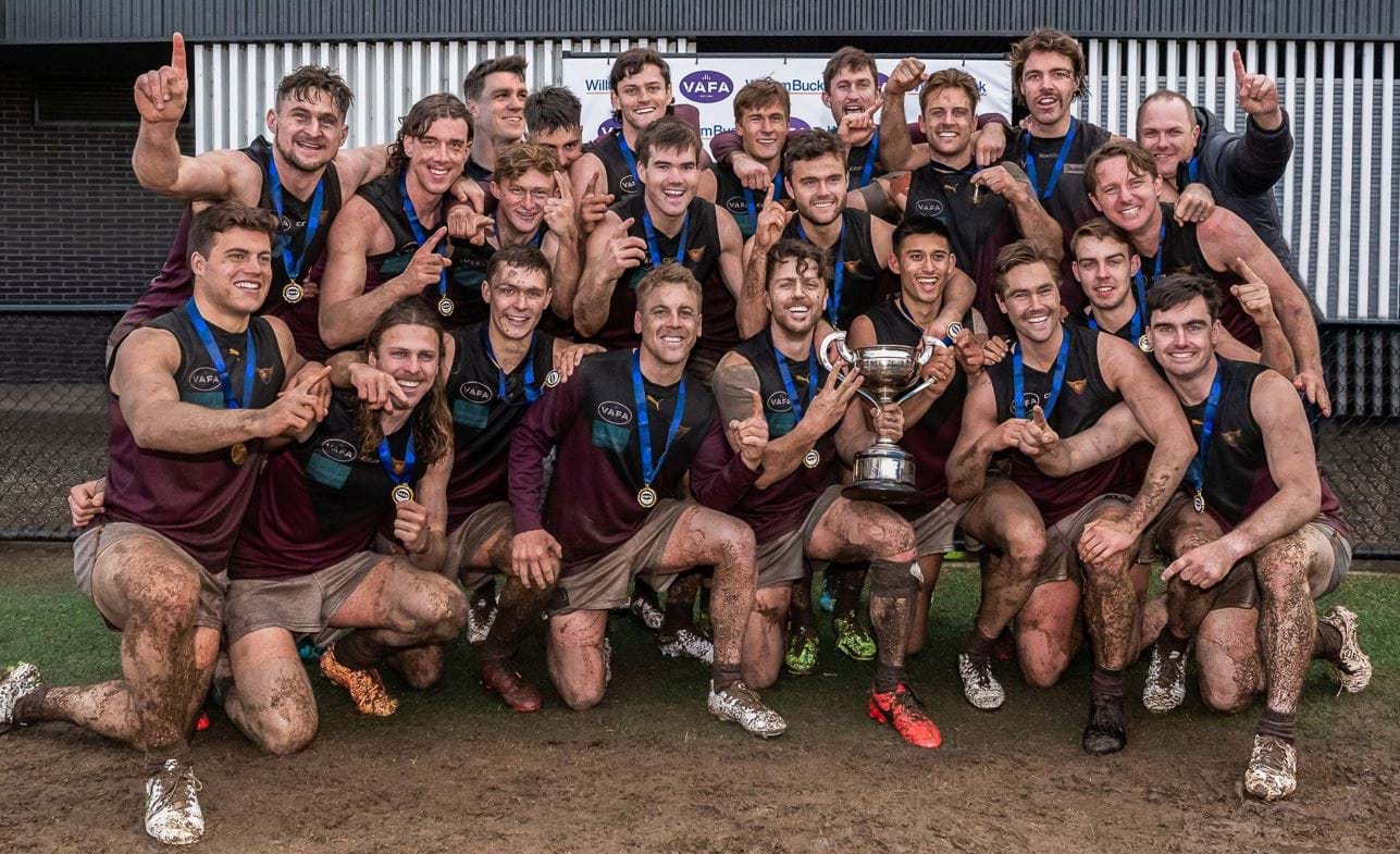 Coach Daniel Ward and his grand mud-spattered team celebrate the Bloods ninth Senior premiership on the soggy Elsternwick Park turf where they prevailed over University Blacks.  Captain James Paul lifts the cup.